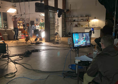 Behind the scenes of a large television commercial. Cast and crew are in the middle of filming and studio lights are on while producers and directors look on